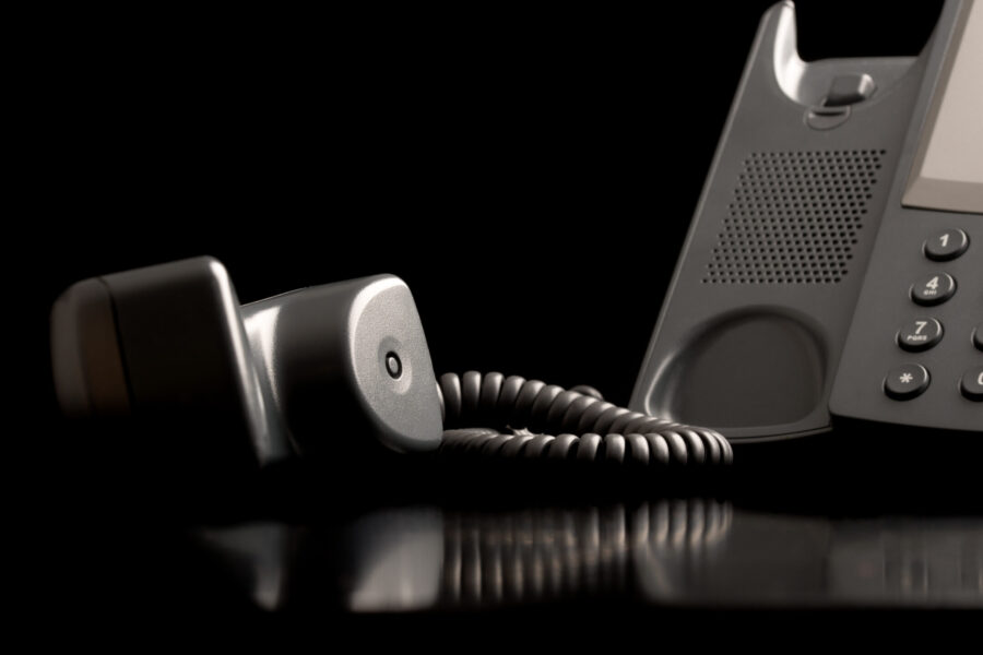 Telephone handset off the hook lying on a black reflective surface alongside the instrument , close up low angle view with copyspace.